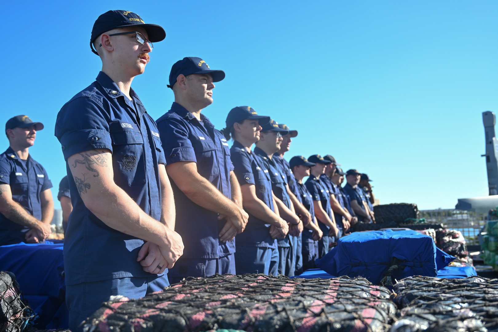 Coast Guard Cutter Stone (WMSL 758) crew members stand before seized contraband during a drug offload at Port Everglades in Fort Lauderdale, Florida, Nov. 19, 2025. Stone’s crew offloaded approximately 49,010 pounds of illicit narcotics worth more than $362 million. (U.S. Coast Guard photo by Petty Officer 2nd Class Brandon Hillard)