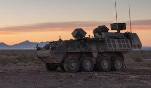 A combat vehicle is outdoors in a desert environment in the evening.
