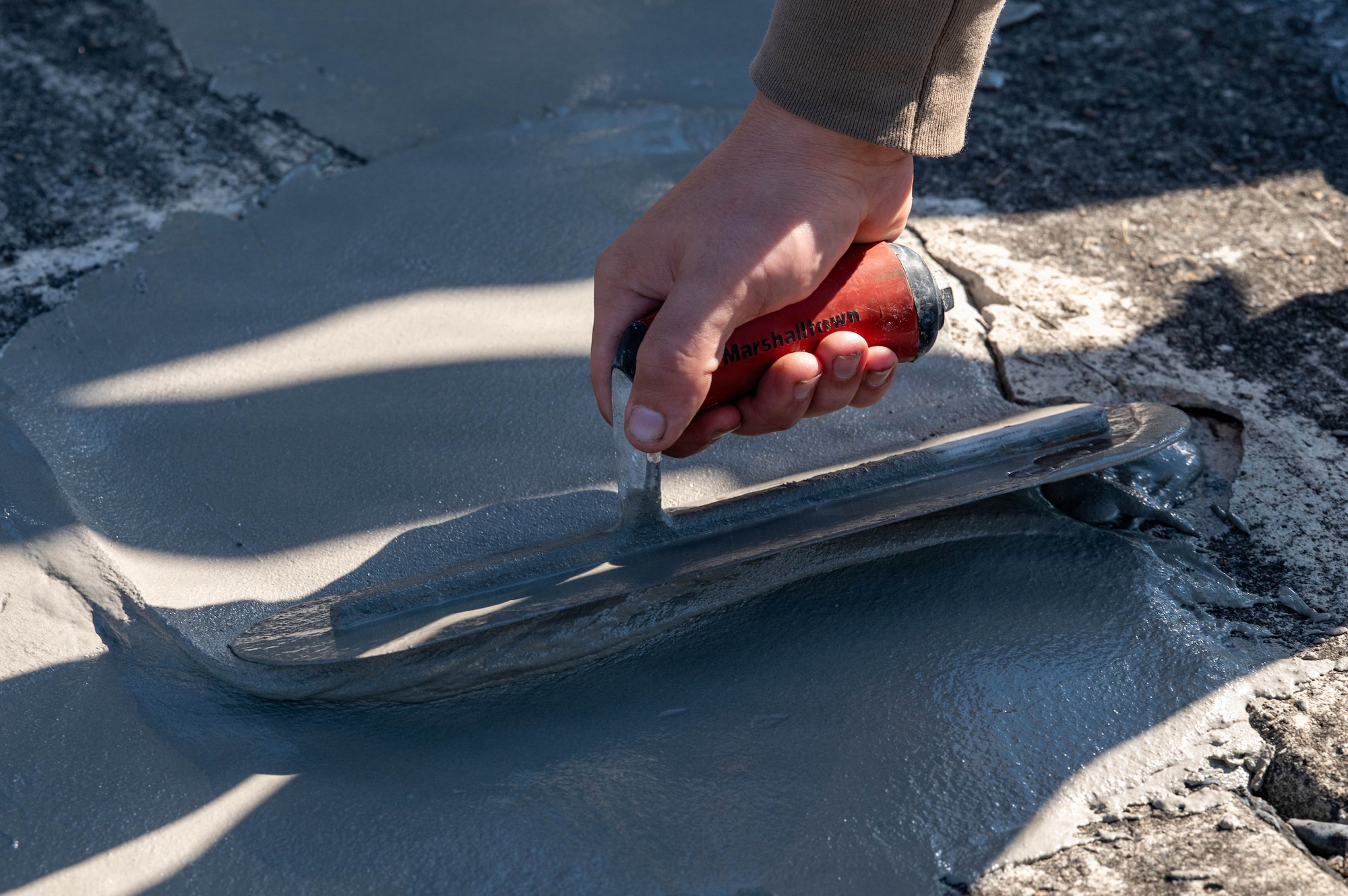 A photo of a hand smoothing concrete with a tool