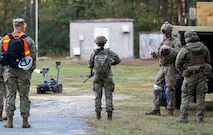 A photo of  Airmen standing in front of a robot with a camera.