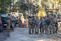 A photo of Airmen standing in a group with other Airmen and equipment behind them.