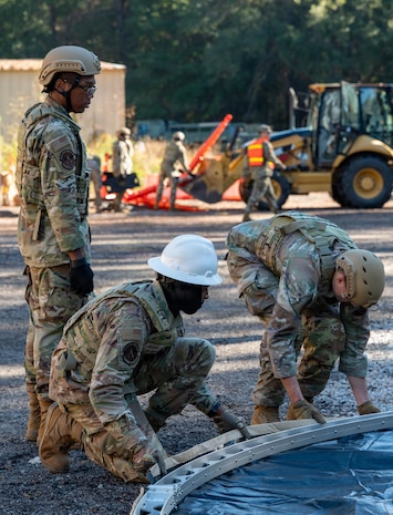 A photo of Airmen building the metal frame of a tent while crouched on the ground