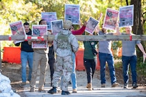 A photo of Airmen holding signs behind a barricade during a protest simulation