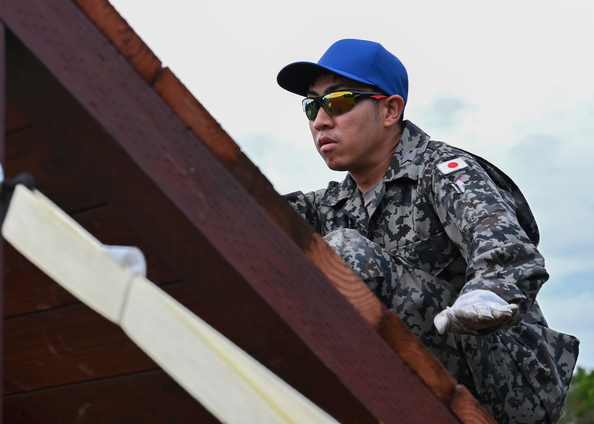 A foreign airman with sunglasses and a blue hat climbs on a platform during Silver Flag.