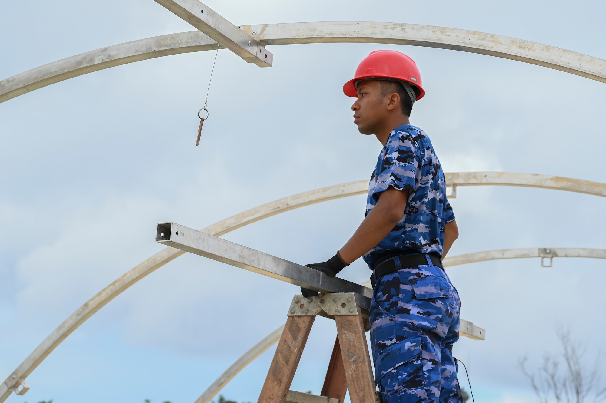 An Indonesian Air Force airman stands on a ladder as he looks at the structure he is working on.
