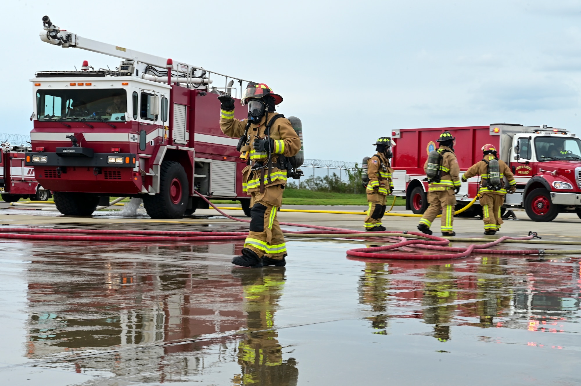 A firefighter makes hand signs by a firetruck.