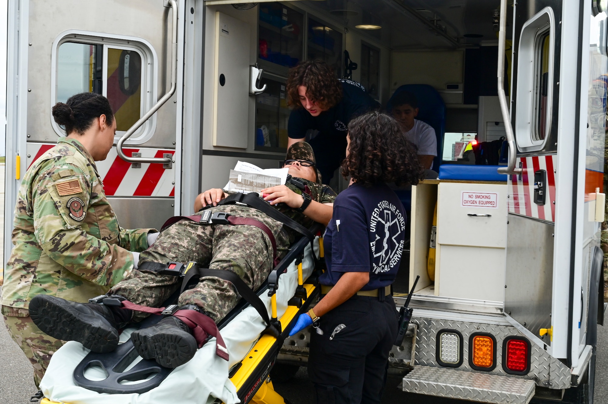 Three people load a stretcher onto an ambulance.