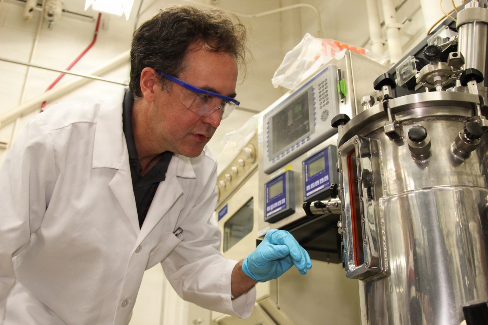 A man in a lab coat interacts with a stainless-steel containment vessel.