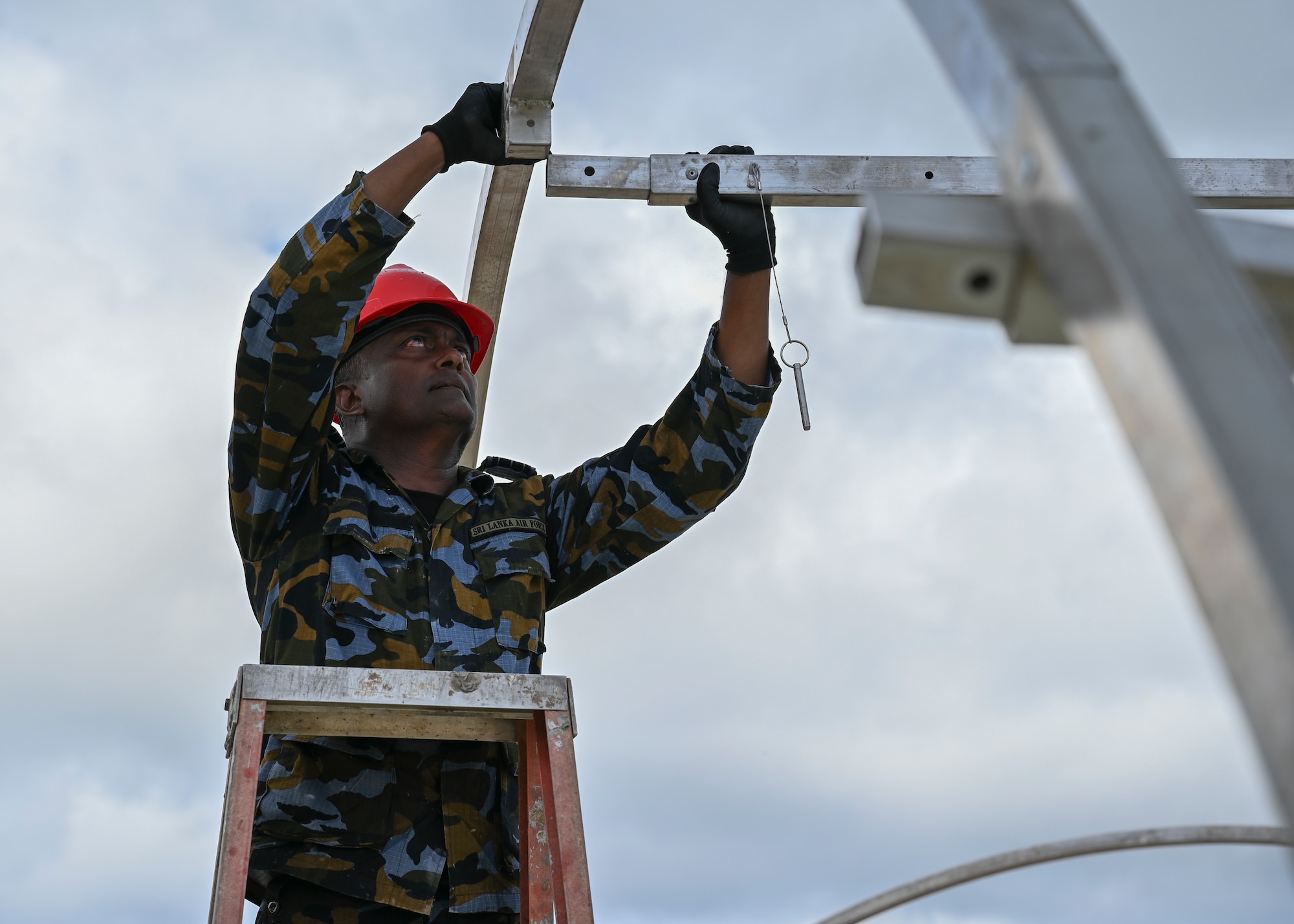 A Sir Lanka Air Force airman stands on a ladder and connects a part of the structure to the other part.