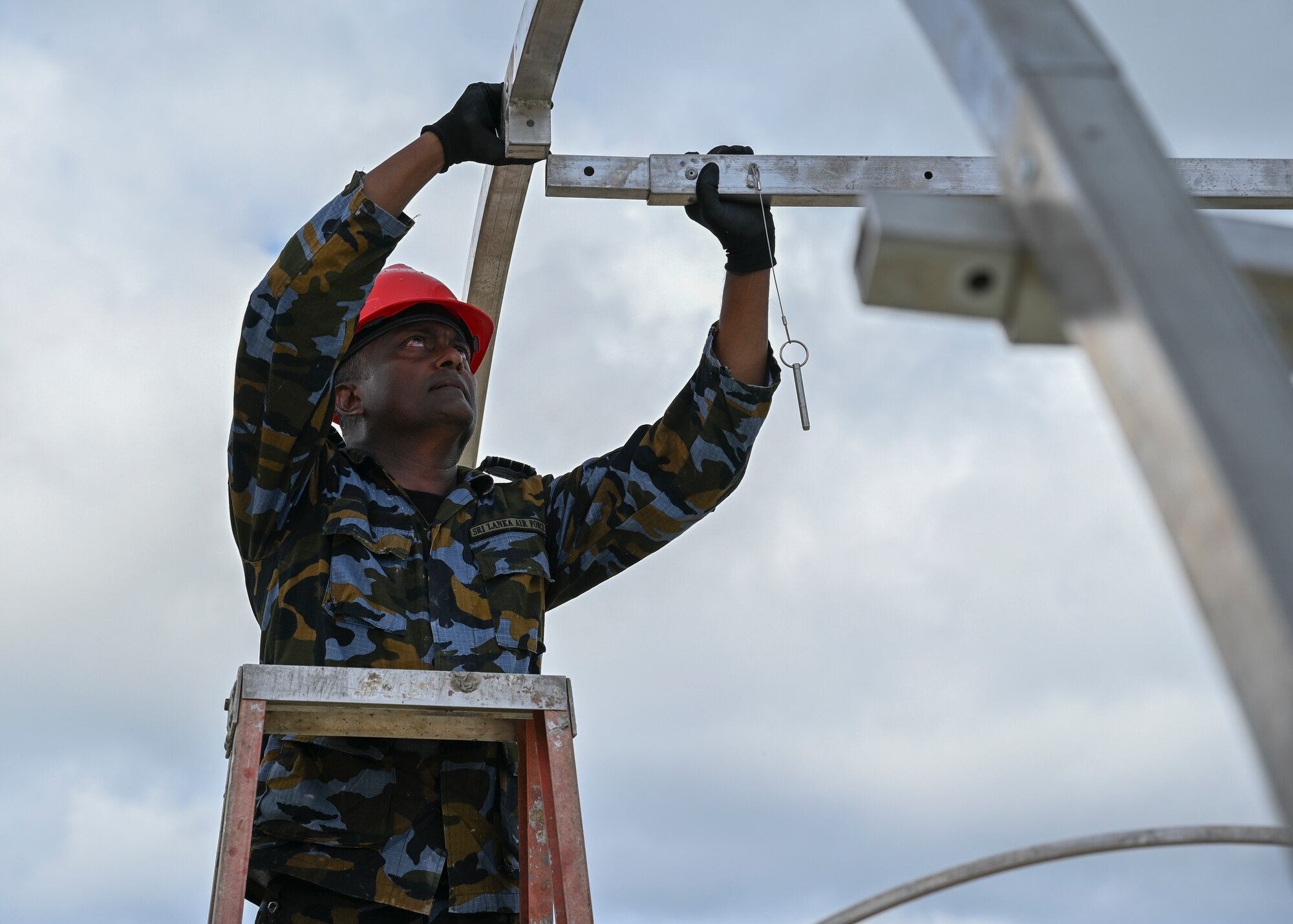 A Sir Lanka Air Force airman stands on a ladder and connects a part of the structure to the other part.