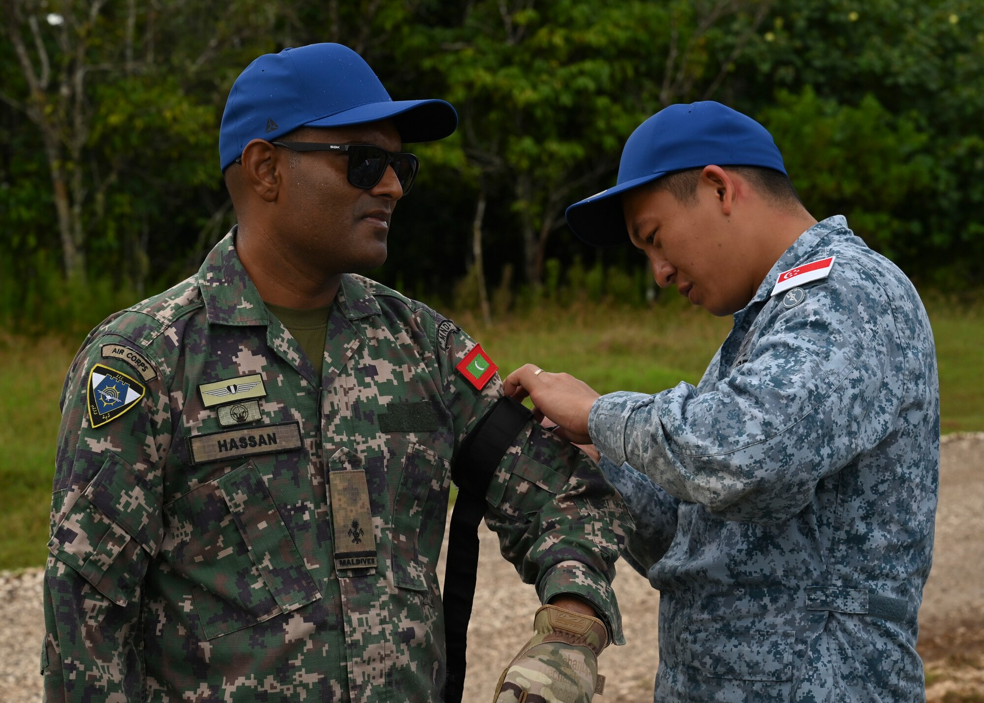A Republic of Singapore Air Force airman with a blue hat practices wrapping a tourniquet around a Maldives National Defense Force airman during PERC.