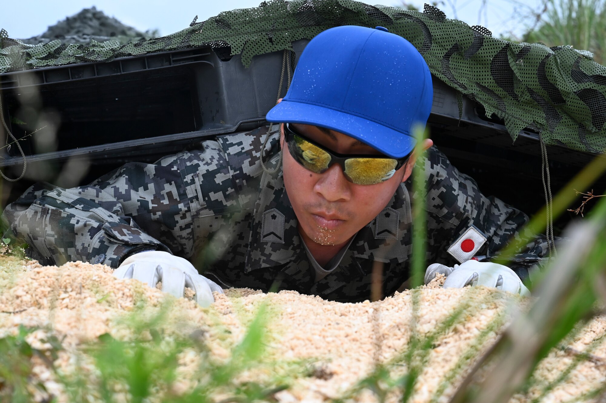 A foreign airman with a blue hat and sunglasses climbs underneath the obstacle course during PERC.