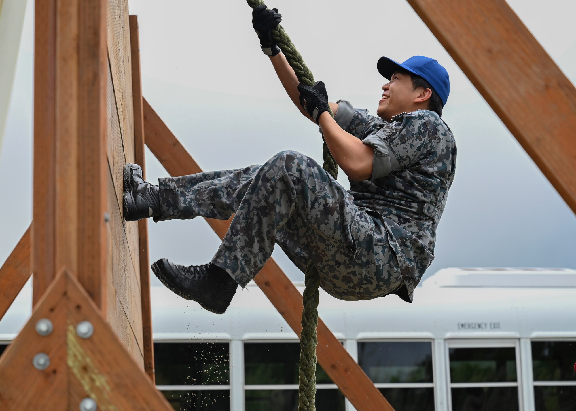 A foreign airman with a blue hat uses a rope to climb up the obstacle course during PERC.