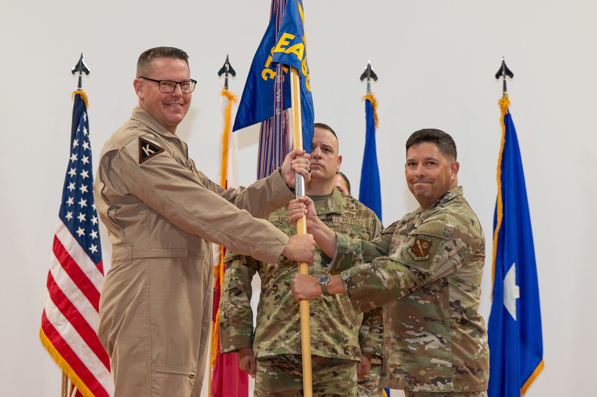 Brig Gen Clayton hands a guidon to Col Trujillo while two people stand at attention behind them.