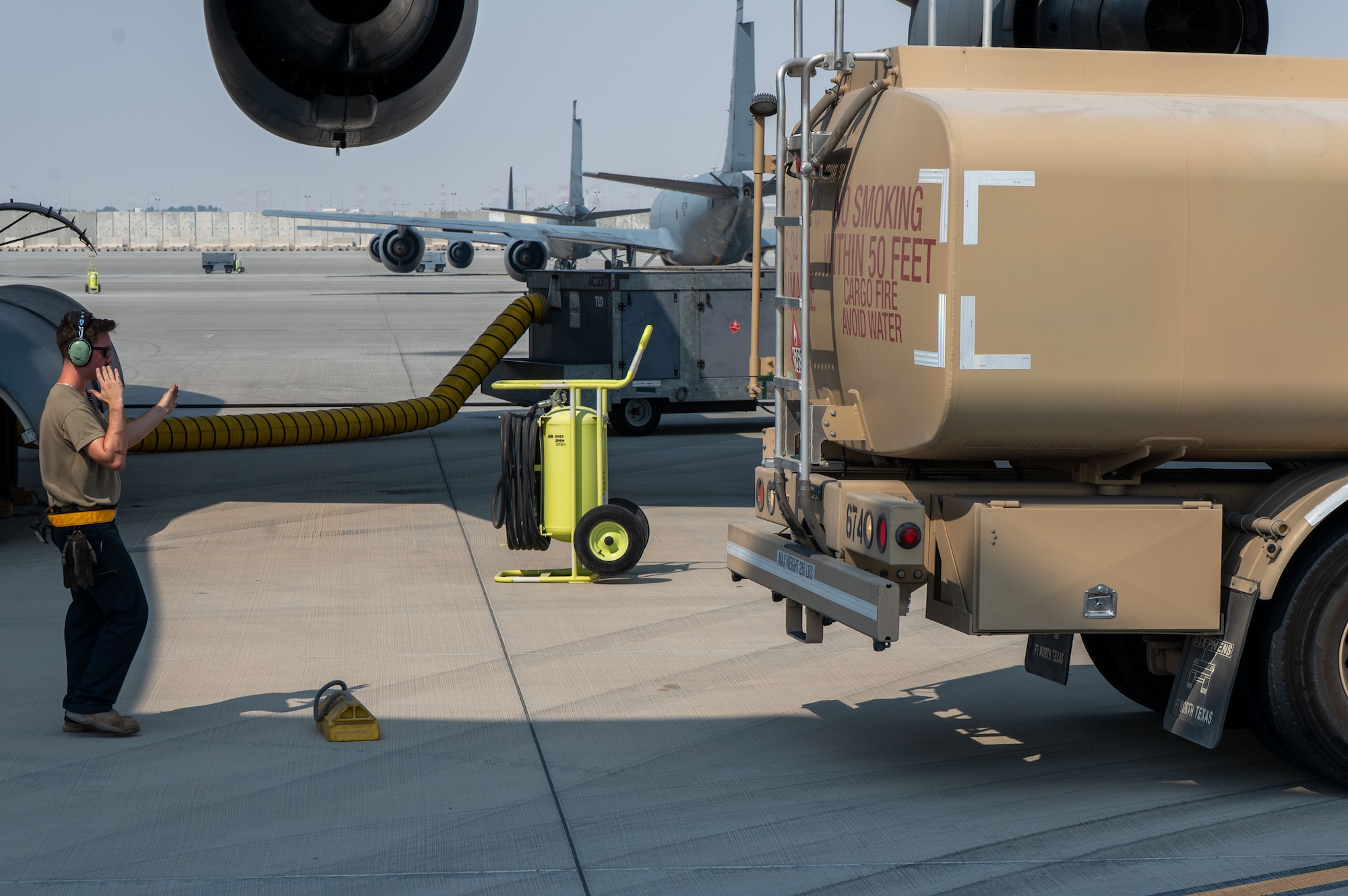 An Airman signals with his hands for a truck to back up to the chock placed on the ground between them