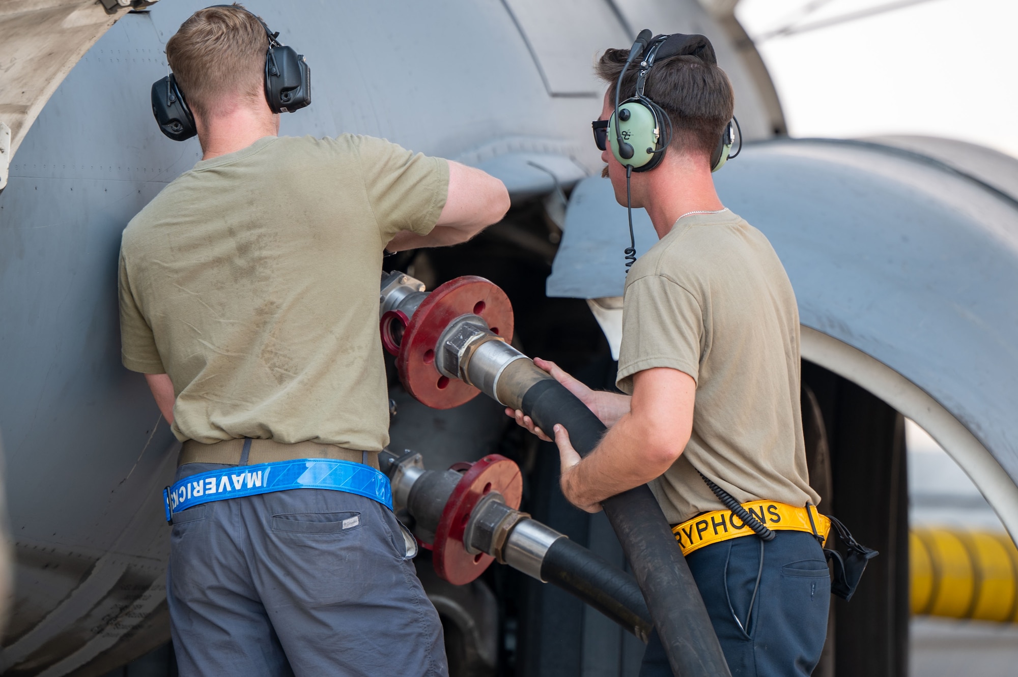 Two Airman work in tandem to connect a fuel hose to an aircraft