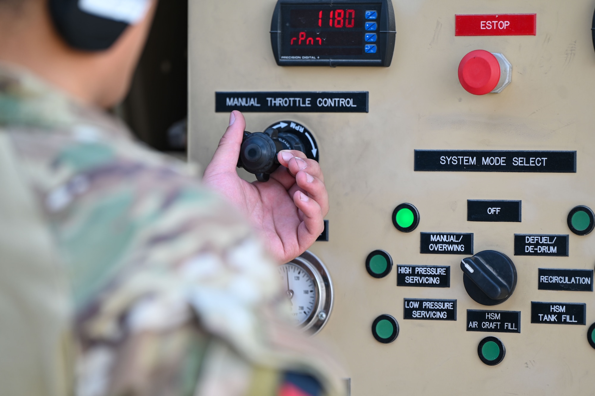 Close up of an Airman's hand turning a throttle control knob on a control panel