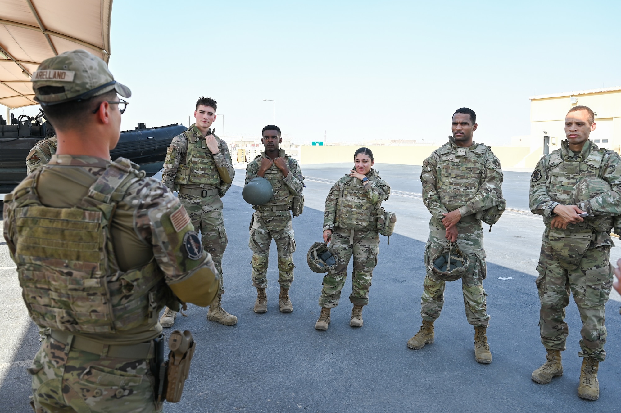 Airmen stand in a circle listening to one speak