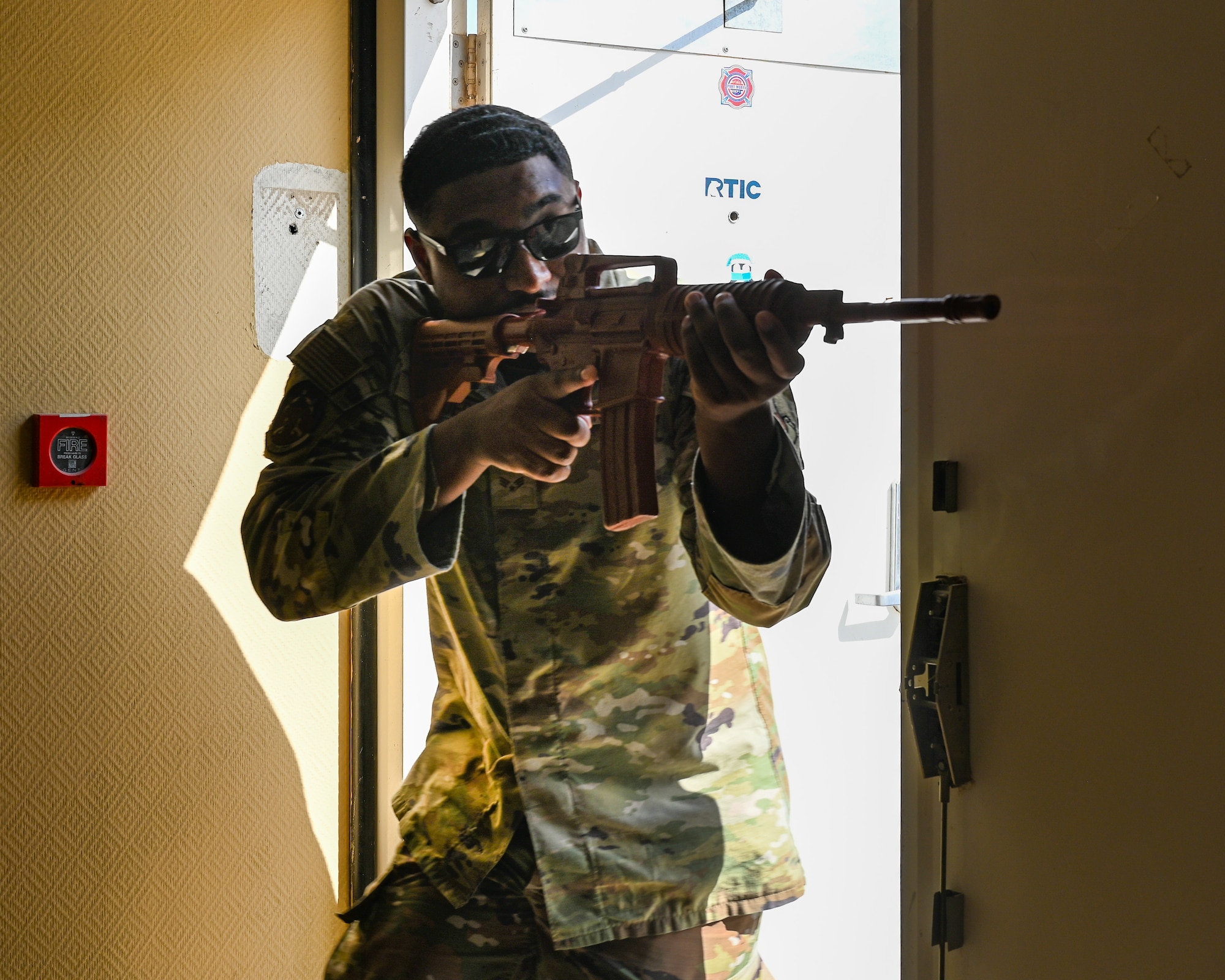 An Airman stands in the frame of a doorway with his simulated weapon up scanning for a simulated active shooter