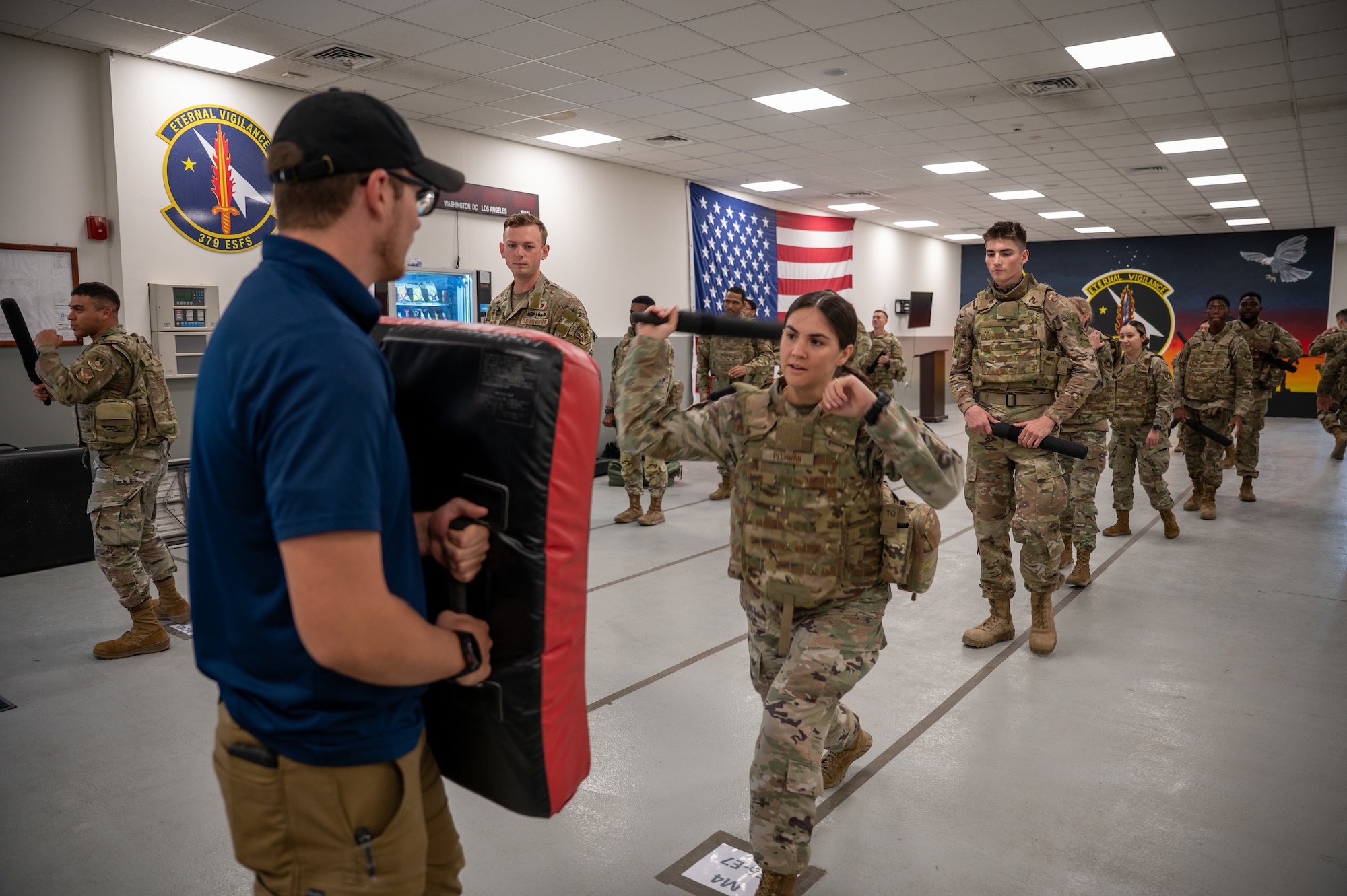 Airmen in two lines look on as the ones in the front strike a padded shield with a foam baton