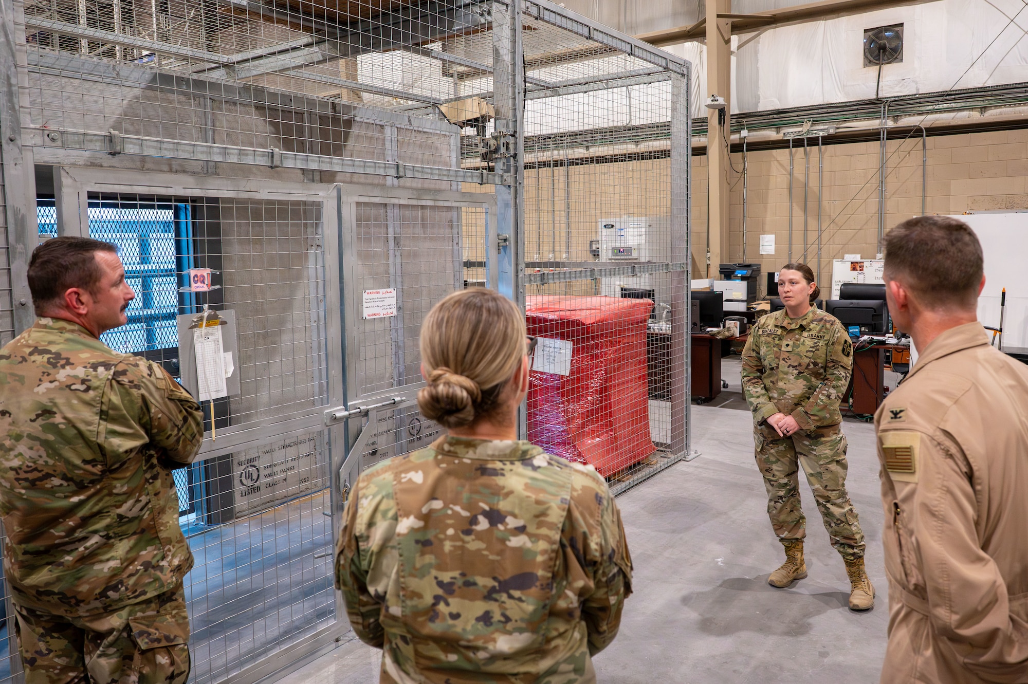 Three U.S. Air Force members stand listening to a Soldier speak outside of a secure storage cage