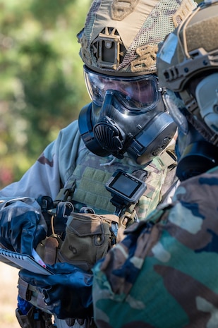 A photo of an Airman in a gas mask and Mission Oriented Protective Posture gear writes on a piece of paper.
