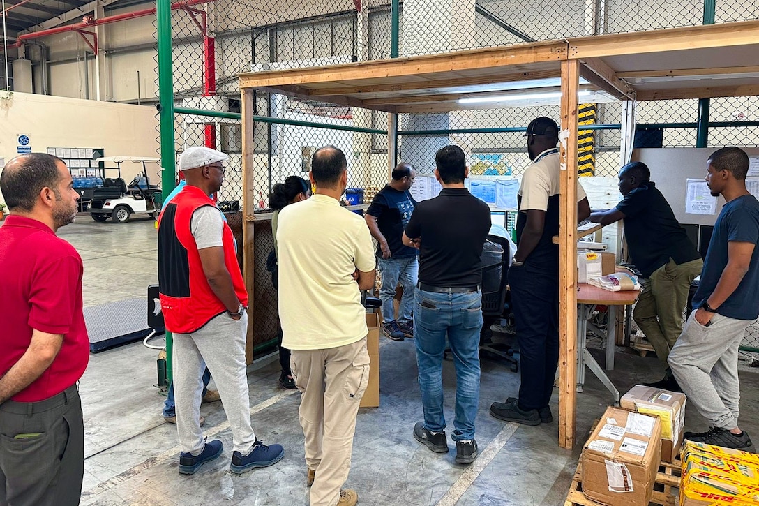 A group of people stand around a workstation inside a warehouse.