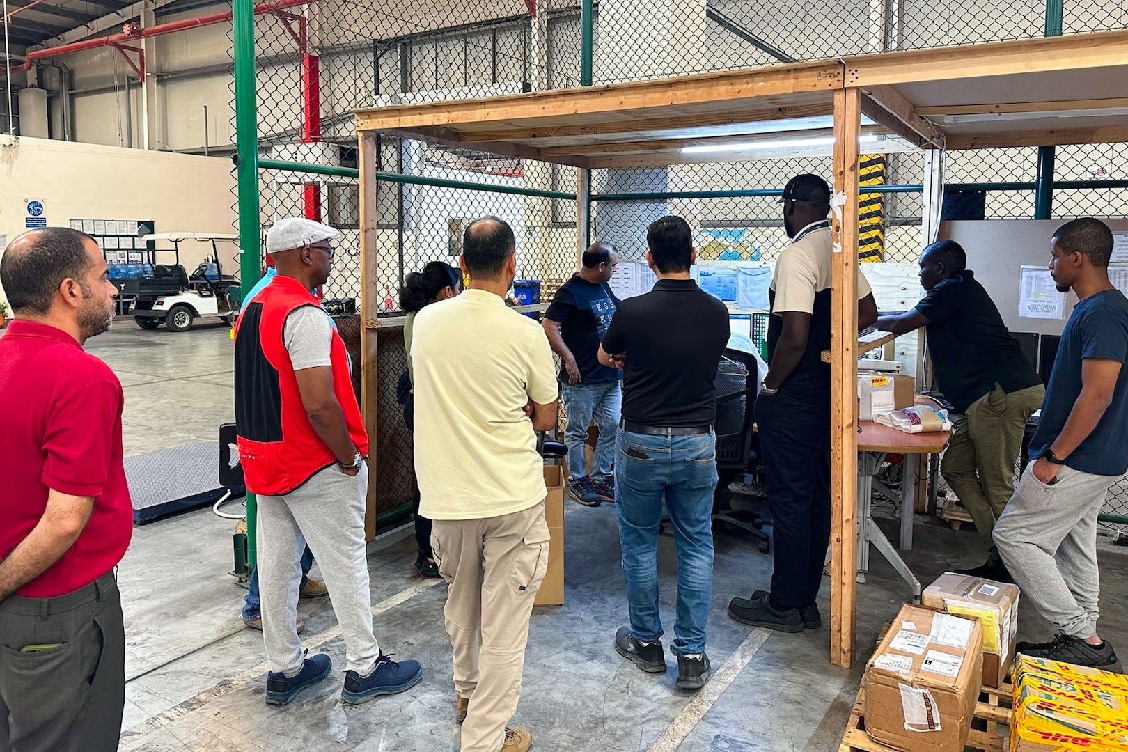 A group of people stand around a workstation inside a warehouse.