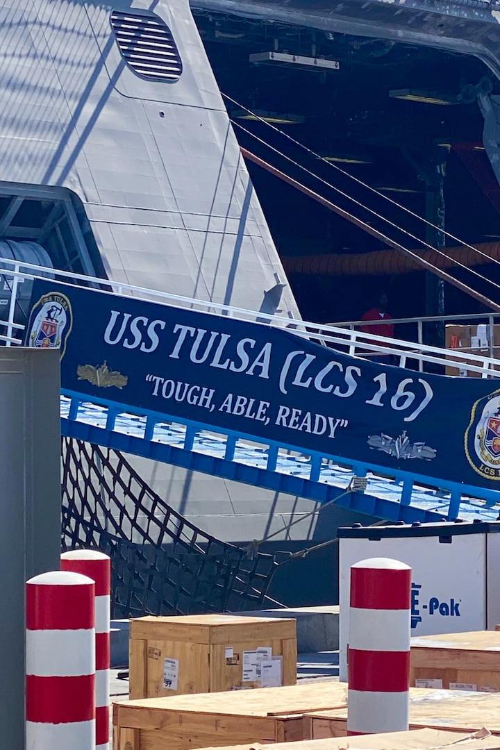 Cargo is loaded onto U.S. Navy Independence-variant littoral combat ship USS Tulsa on a sunny day. There is a banner that reads 'USS TULSA (LCS 16) Tough, Able, Ready'.