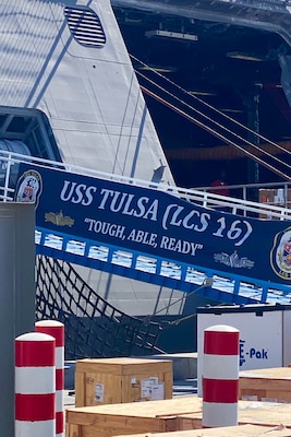 Cargo is loaded onto U.S. Navy Independence-variant littoral combat ship USS Tulsa on a sunny day. There is a banner that reads 'USS TULSA (LCS 16) Tough, Able, Ready'.
