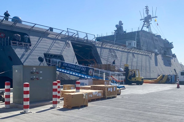 Cargo is loaded onto U.S. Navy Independence-variant littoral combat ship USS Tulsa on a sunny day.