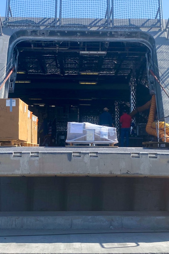 Cargo sits outside of a U.S. Navy Independence-variant littoral combat ship on a sunny day.