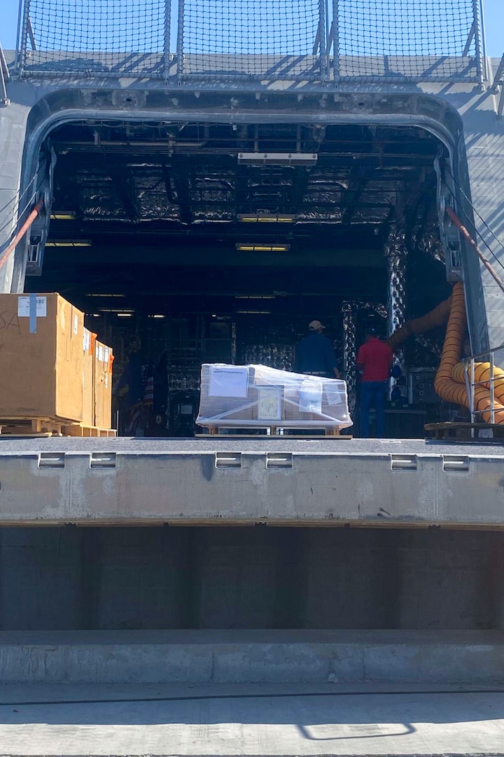 Cargo sits outside of a U.S. Navy Independence-variant littoral combat ship on a sunny day.