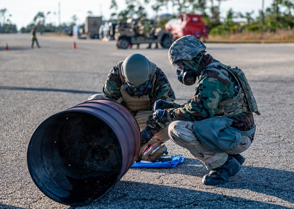 U.S. Air Force Airmen conduct a “buddy check” after donning their chemical protective gear after a simulated chemical attack during exercise Mosaic Tiger 26-1 at the Combat Support Training Range at Tyndall Air Force Base, Florida, Nov. 18, 2025. The gear protects members from most contaminants of biological, chemical and radiological threats, and the “buddy checks” aim to ensure that the gear is worn properly. (U.S. Air Force photo by Senior Airman Leonid Soubbotine)