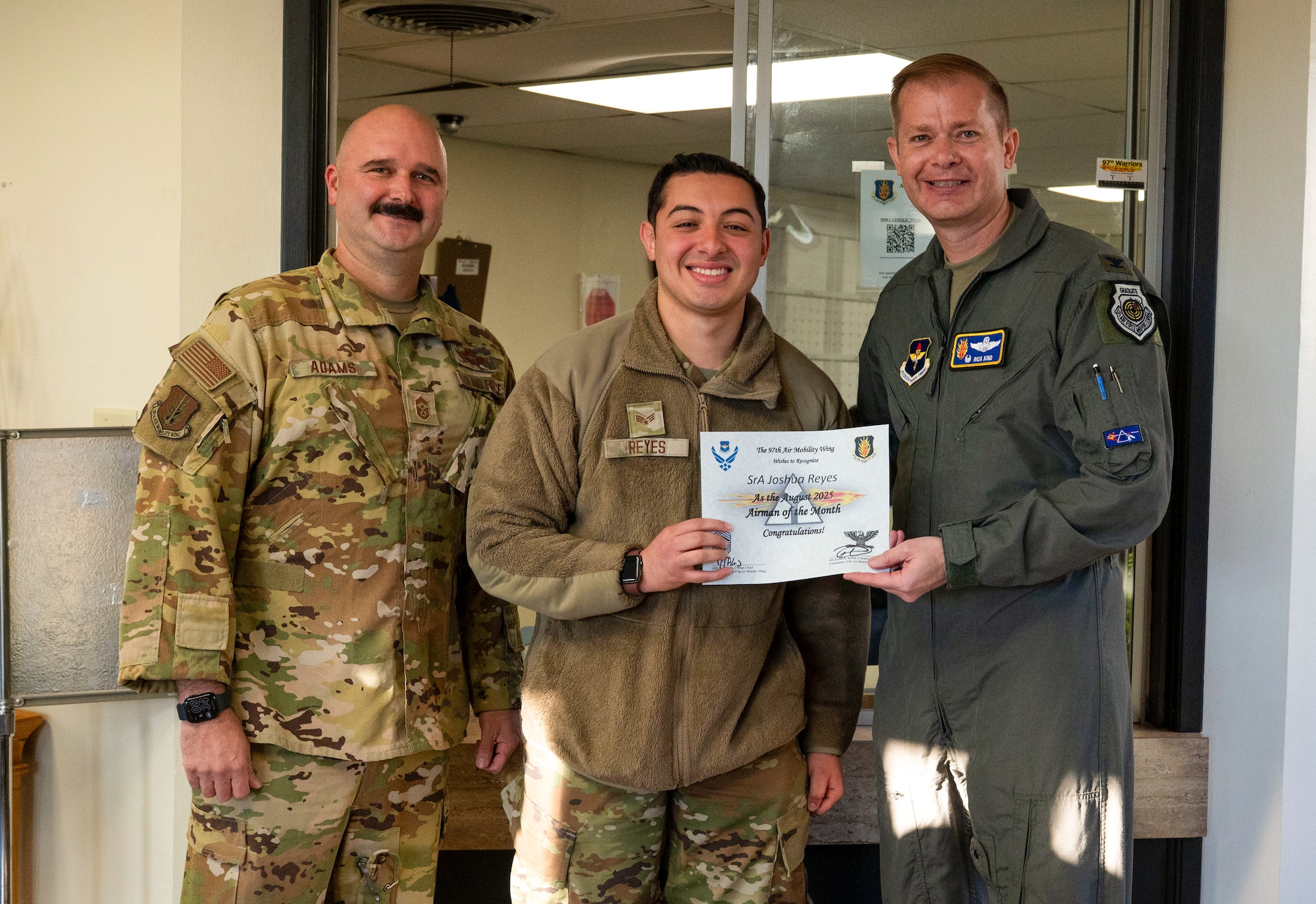 U.S. Air Force Col. Richard Kind, right, 97thAir Mobility Wing (AMW) commander , and Chief Master Sgt. Jonny Adams, left, 97thAMW command chief, hands an award to Senior Airman Joshua Reyes, center, 97thAMW Chapel Office religious affairs airman, at Altus Air Force Base, Oklahoma, Sept. 29,2025. Reyes was named the Airman of the Month for August 2025. (U.S. Air Force photo by Tech. Sgt. Hailey Haux)