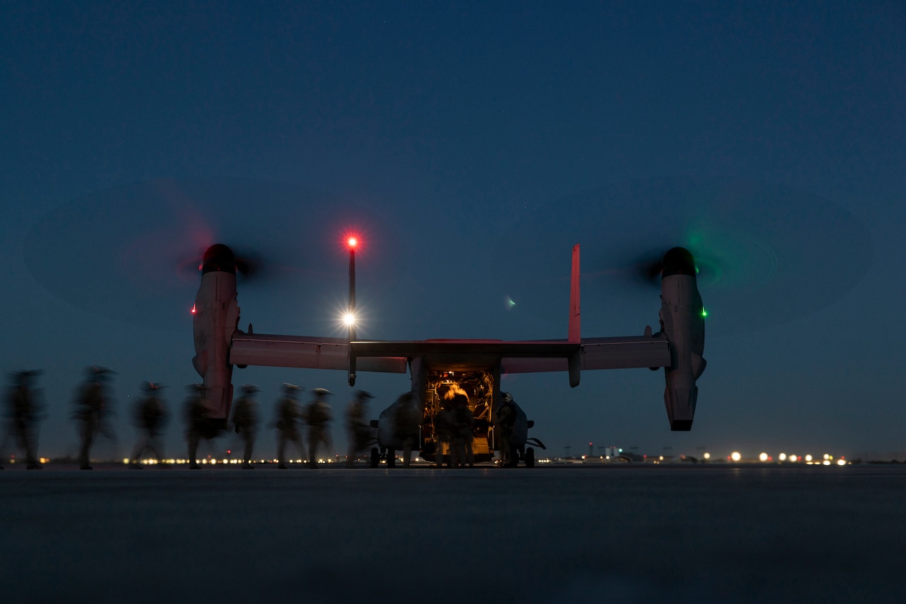A military aircraft sits on a dark flight line as service members board the aircraft.