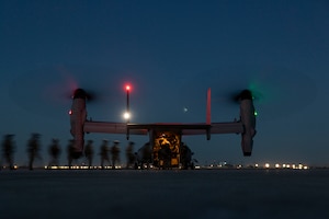 A military aircraft sits on a dark flight line as service members board the aircraft.