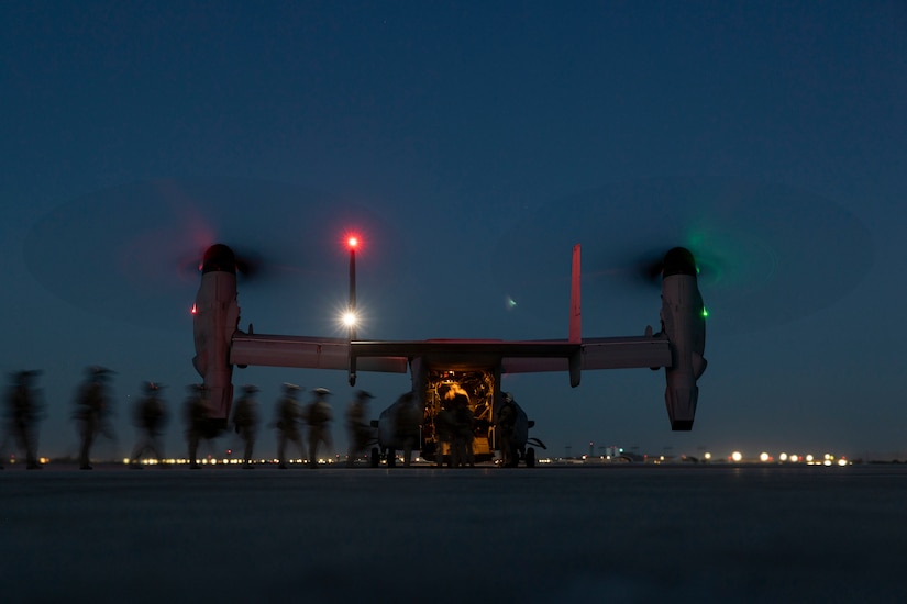 A military aircraft sits on a dark flight line as service members board the aircraft.