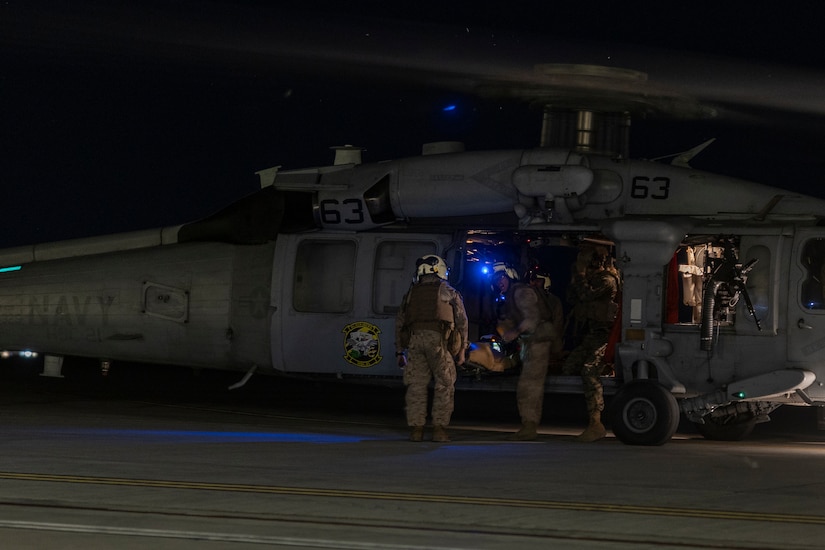Service members wearing flight suits load a person onto a military aircraft during a simulated nighttime rescue operation.