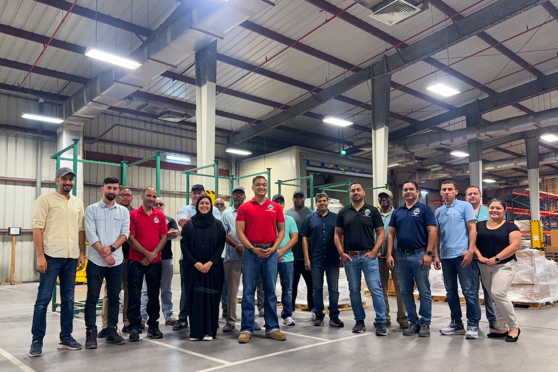 A group of people stand for a group photo inside a warehouse.