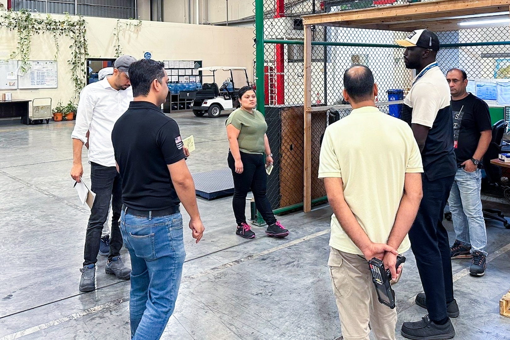 A group of people stand around a workstation inside a warehouse.