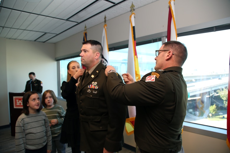 Maj. Matthew Westcott stands at attention while his wife Louise Westcott and U. S. Army Col. Brandon Bowman, U.S. Army Corps of Engineers Jacksonville District Commander pin on his new rank during the promotion of Westcott to Lieutenant Colonel during a promotion ceremony Nov. 13, at the District Headquarters in the Prudential Building.  As Westcott prepares to ascend to the next echelon of leadership within USACE, his promotion is a testament to his unwavering commitment and meritorious service.  (U.S. Army photo by Mark Rankin)