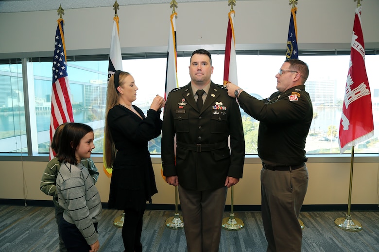 Maj. Matthew Westcott stands at attention while his wife Louise Westcott and U. S. Army Col. Brandon Bowman, U.S. Army Corps of Engineers Jacksonville District Commander pin on his new rank during the promotion of Westcott to Lieutenant Colonel during a promotion ceremony Nov. 13, at the District Headquarters in the Prudential Building.  As Westcott prepares to ascend to the next echelon of leadership within USACE, his promotion is a testament to his unwavering commitment and meritorious service.  (U.S. Army photo by Mark Rankin)