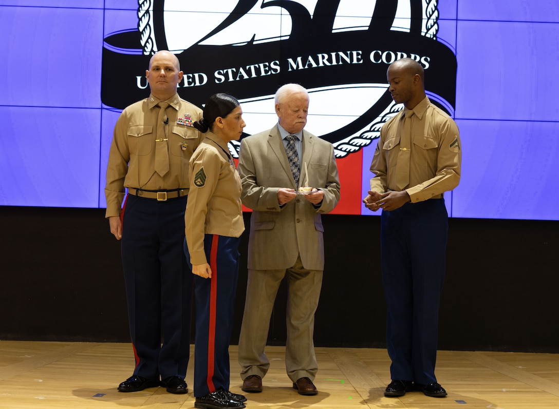 Three men on stage with woman in uniform in front of them standing at attention facing right