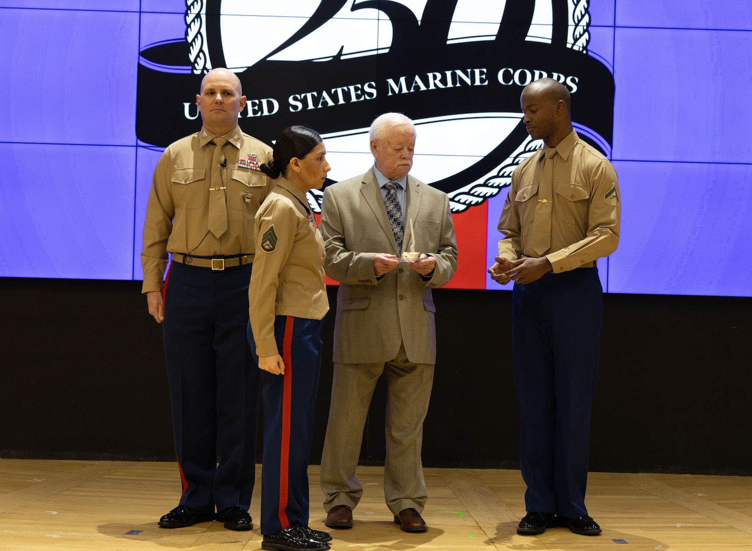 Three men on stage with woman in uniform in front of them standing at attention facing right