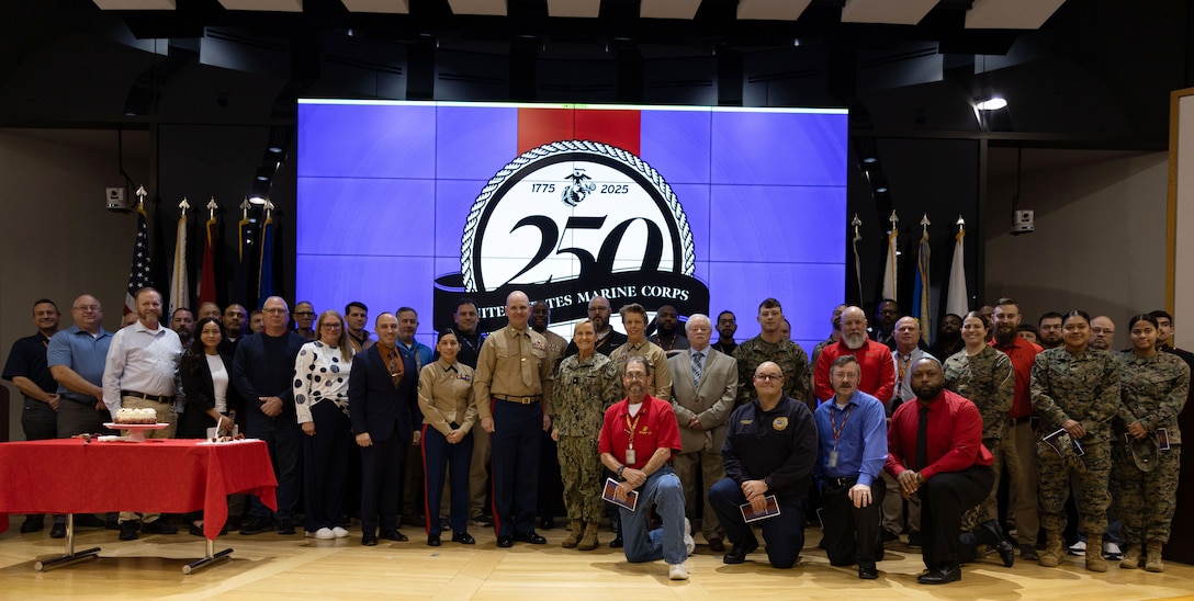Large group of people pose for a photo on stage - some in uniform some in civilian attire.