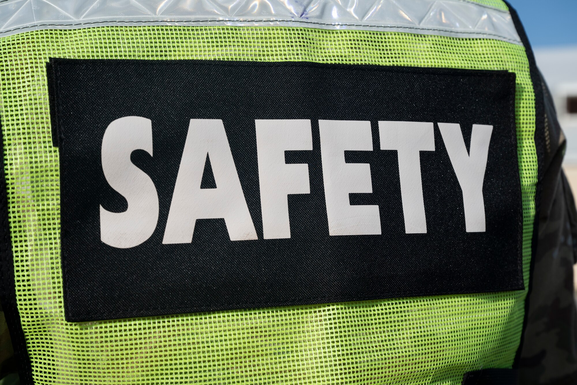 A person wears a neon-yellow vest displaying the word 'Safety' in large white letters