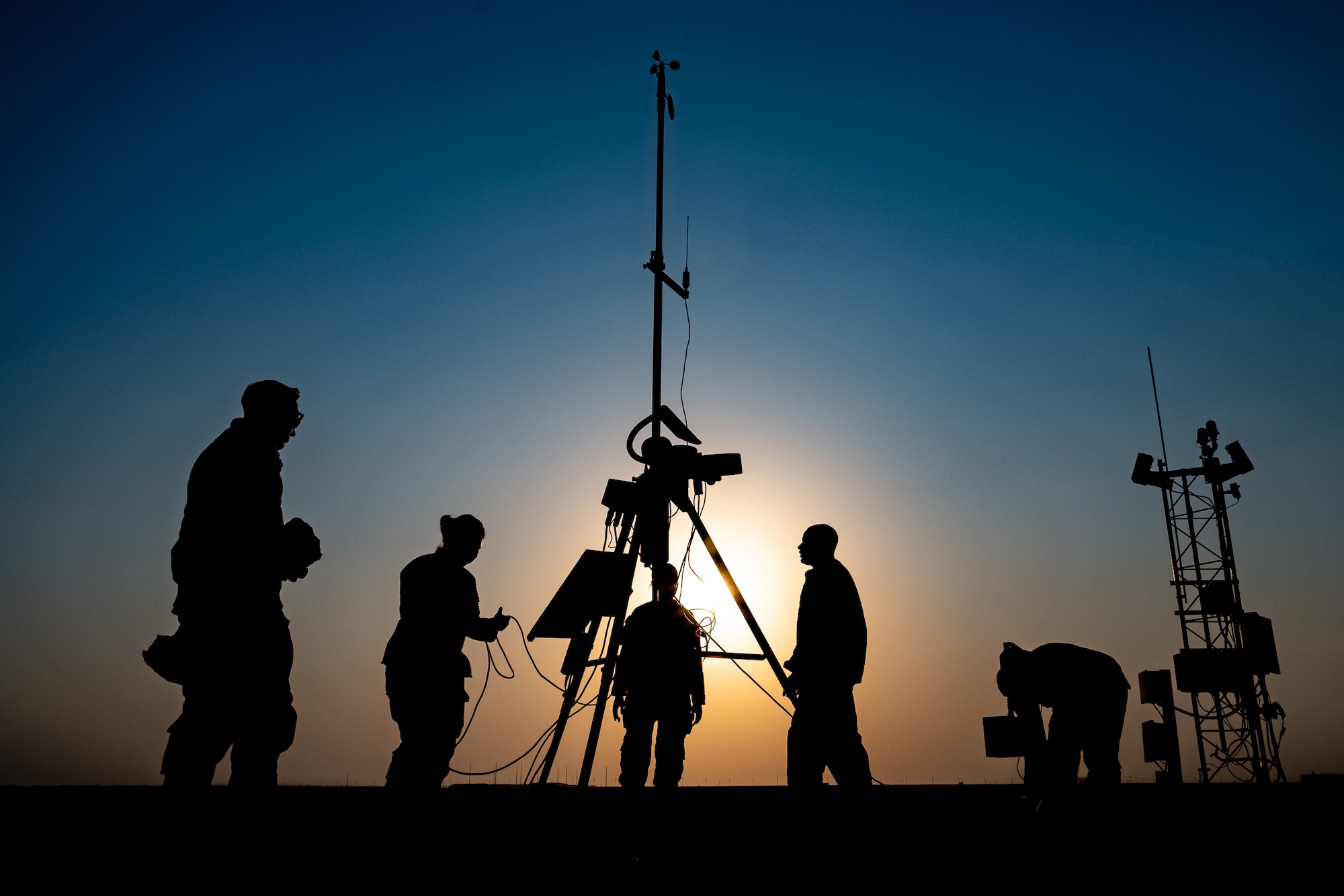 Five Airmen and a sensor are silhouetted against the sun