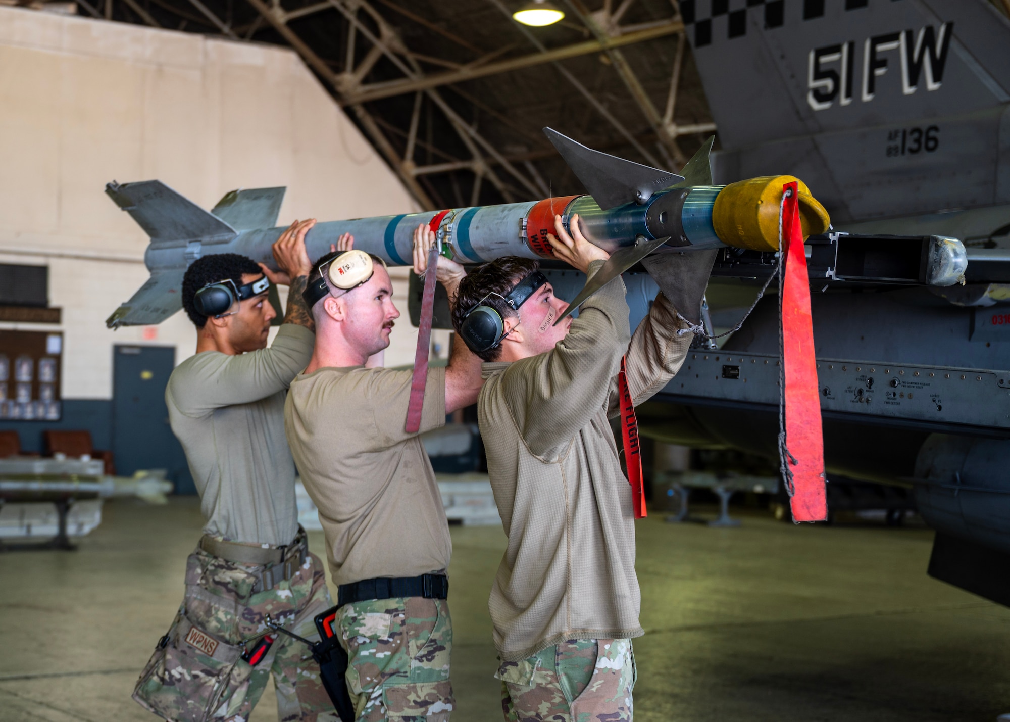 Airmen assigned to the 36th Fighter Generation Squadron lift an AIM-9L/M during a weapons loading competition at Osan Air Base, Republic of Korea, Oct. 2, 2025. Each team consisted of three Airmen: the one-man served as the team chief who supervised the load, the two-man acted as the primary loader responsible for handling the munitions, and the three-man assisted with tools and equipment to ensure a safe, accurate, and efficient load. (U.S. Air Force photo by Staff Sgt. Sarah Williams)