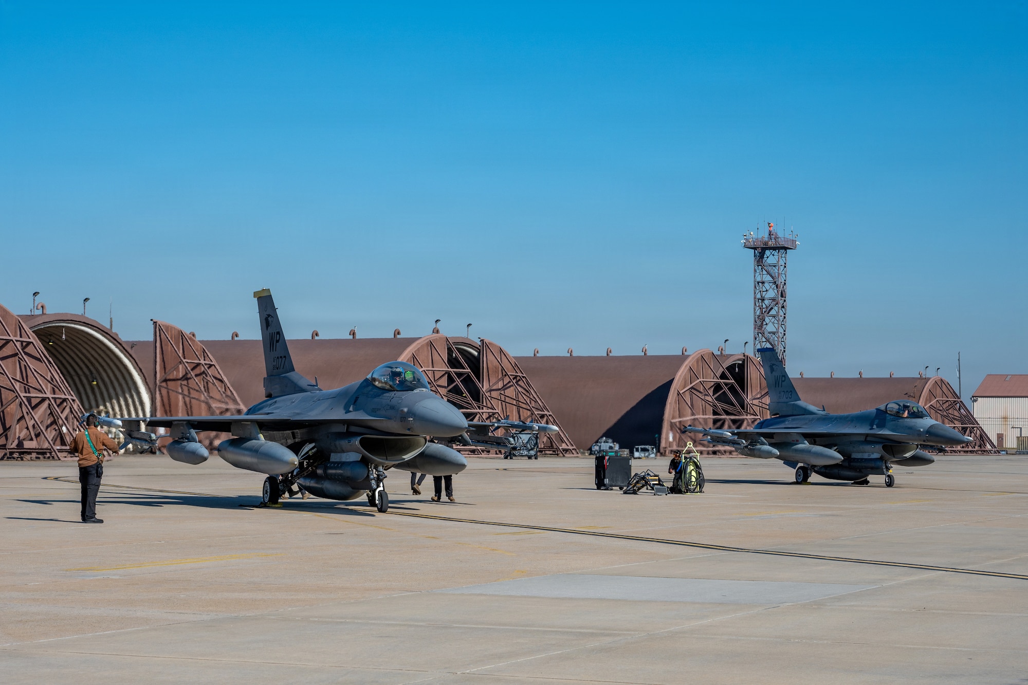 Two F-16s are parked on a taxiway.